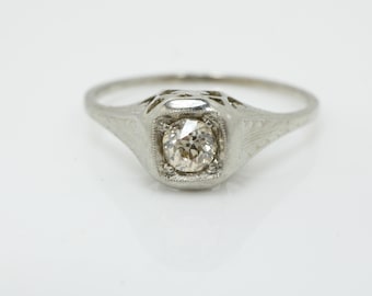 May include: A silver ring with a delicate filigree design and a single round diamond in the center.