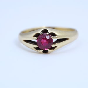 May include: A gold ring with a single, round, red gemstone set in a decorative, open-work setting.
