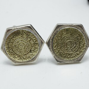May include: A pair of gold and silver cufflinks with a hexagonal shape and a detailed design. The cufflinks feature a circular pattern with intricate details.
