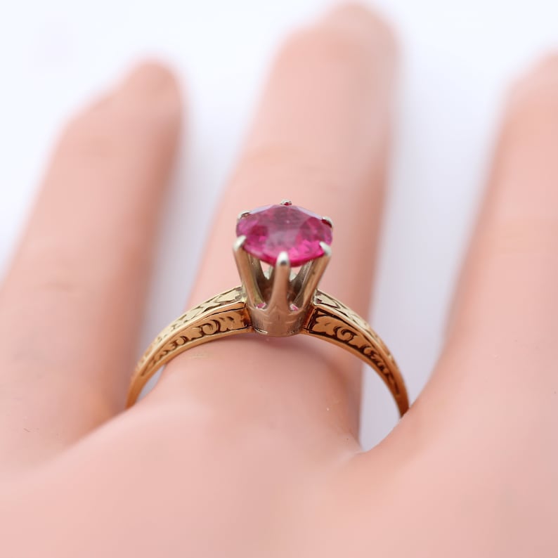 May include: A gold ring with an ornate design and a pink gemstone in the centre.