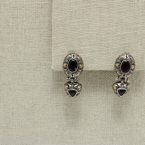May include: A pair of silver and gold earrings with black gemstones. The earrings have a detailed design and are a classic style.