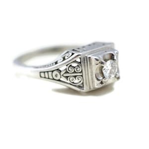 May include: A silver ring with a delicate filigree design and a single round diamond in the center.