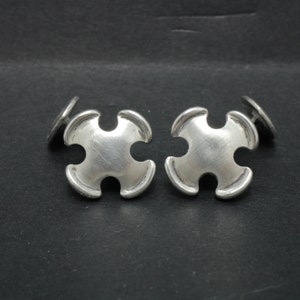 May include: A pair of silver cufflinks in the shape of a four-pointed star with rounded edges.