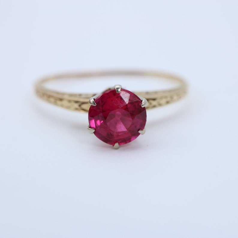 May include: A gold ring with a bright pink gemstone set in a prong setting.