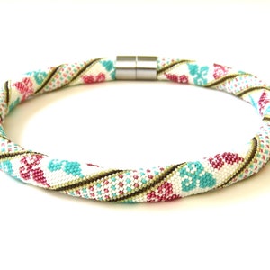 May include: A white beaded necklace with a geometric pattern in shades of pink, turquoise, and brown. The necklace has a magnetic clasp.
