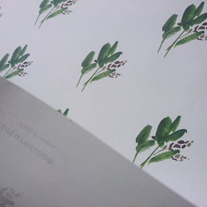 May include: A white background with a repeating pattern of green leafy branches with brown flower buds.