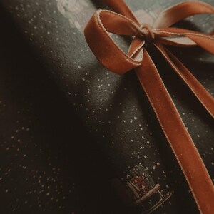 May include: A brown velvet ribbon tied in a bow on top of a dark blue gift wrap with a white snowflake pattern.