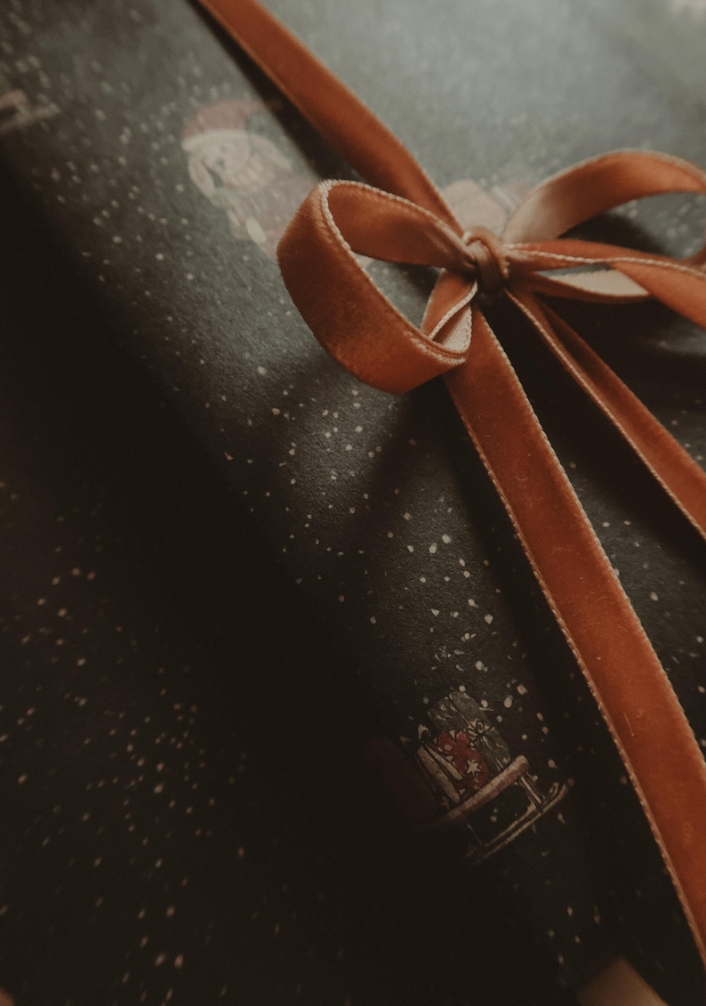 May include: A brown velvet ribbon tied in a bow on top of a dark blue gift wrap with a white snowflake pattern.