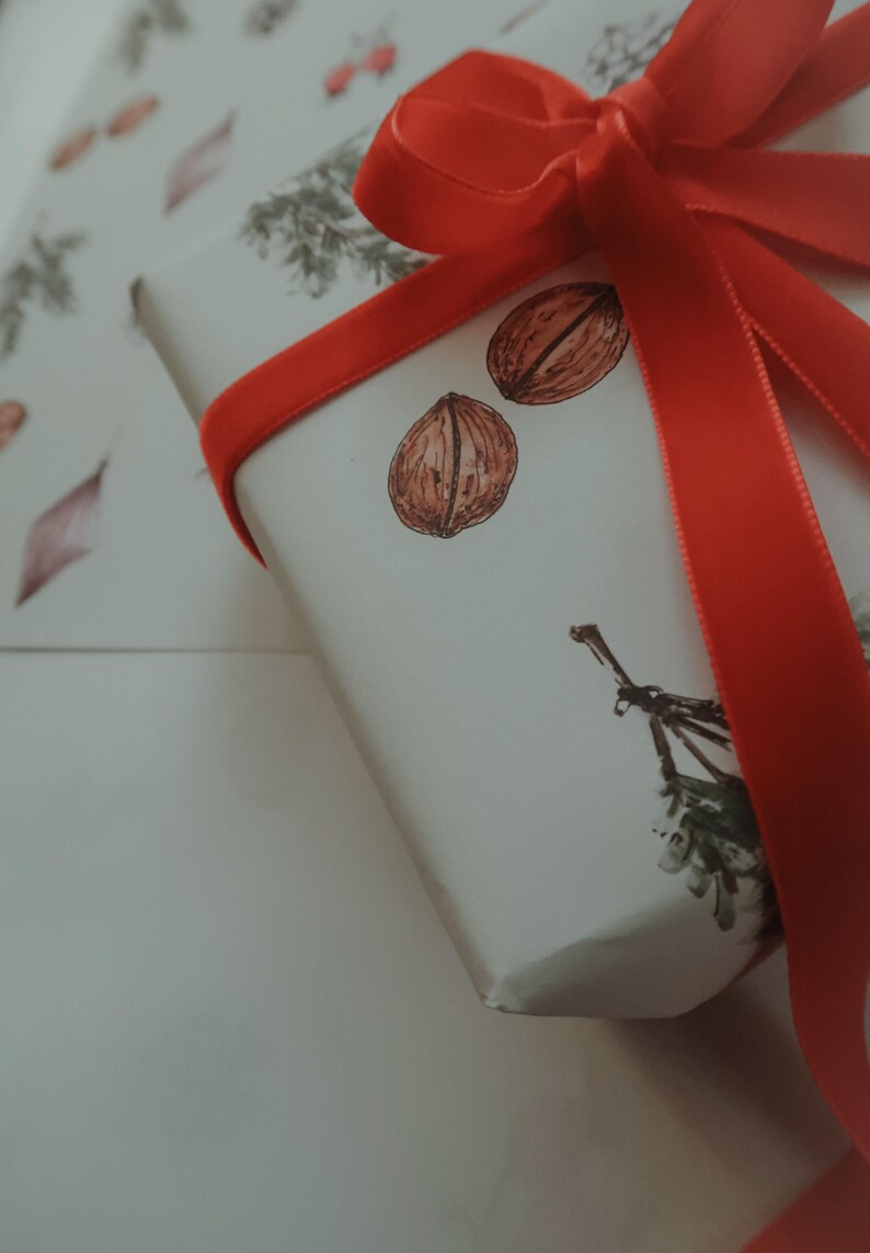 May include: A white gift box with a red ribbon tied in a bow. The box is decorated with a simple design of nuts and leaves.