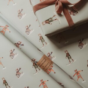 May include: Gift wrap featuring a repeating pattern of skiers in winter attire on a light gray background. A wrapped gift box with a brown velvet ribbon sits atop the wrapping paper. A small tag is visible.