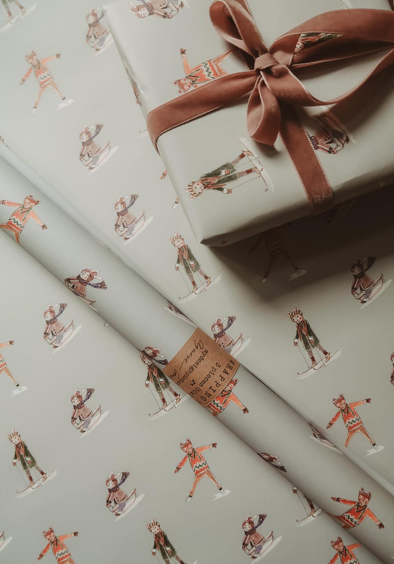 May include: Gift wrap featuring a repeating pattern of skiers in winter attire on a light gray background. A wrapped gift box with a brown velvet ribbon sits atop the wrapping paper. A small tag is visible.