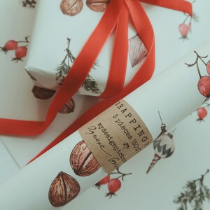 May include: A roll of white wrapping paper with a brown label that says "TRAPPING 3 pieces (50cm)" and "mydesignpictures" with a red ribbon tied around it. The wrapping paper has a pattern of walnuts, red berries, and pine branches.