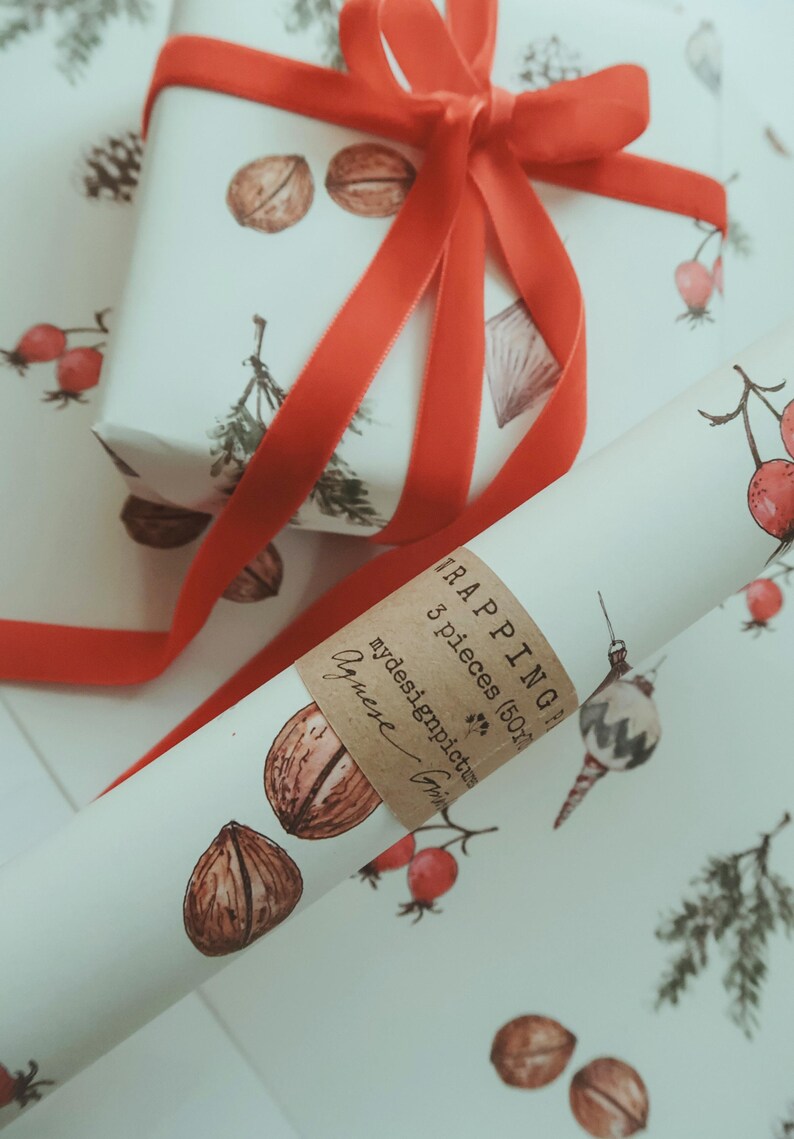 May include: A roll of white wrapping paper with a brown label that says "TRAPPING 3 pieces (50cm)" and "mydesignpictures" with a red ribbon tied around it. The wrapping paper has a pattern of walnuts, red berries, and pine branches.