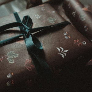 May include: A brown gift box with a green ribbon tied in a bow. The box is wrapped in paper with a floral pattern.