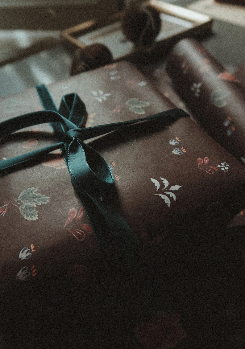 May include: A brown gift box with a green ribbon tied in a bow. The box is wrapped in paper with a floral pattern.