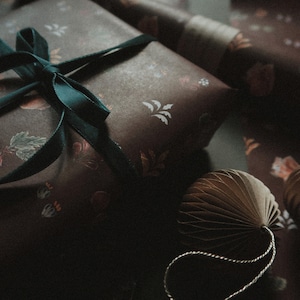 May include: A dark brown gift box with a teal ribbon and a floral pattern. The box is wrapped in paper with a delicate floral design.