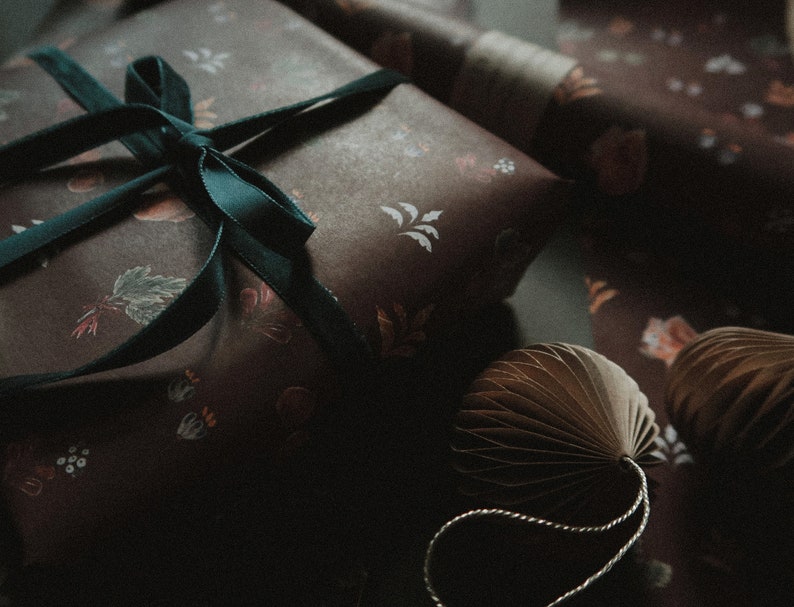 May include: A dark brown gift box with a teal ribbon and a floral pattern. The box is wrapped in paper with a delicate floral design.