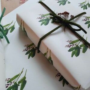 May include: Two rolls of white wrapping paper with a green floral pattern. The paper is tied with a green ribbon and a small sprig of dried flowers.