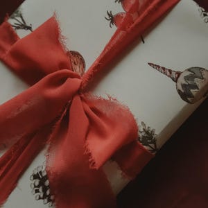 May include: A white gift box with a red ribbon tied in a bow. The box is decorated with a watercolor pattern of berries, leaves, and ornaments.
