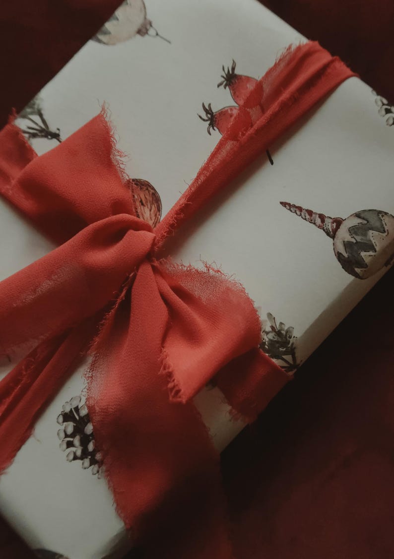 May include: A white gift box with a red ribbon tied in a bow. The box is decorated with a watercolor pattern of berries, leaves, and ornaments.
