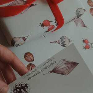 May include: White wrapping paper with a red ribbon tied in a bow. The paper has a repeating pattern of Christmas ornaments, pine cones, and red berries. The text "MyBestPrints.com" is printed on the paper.