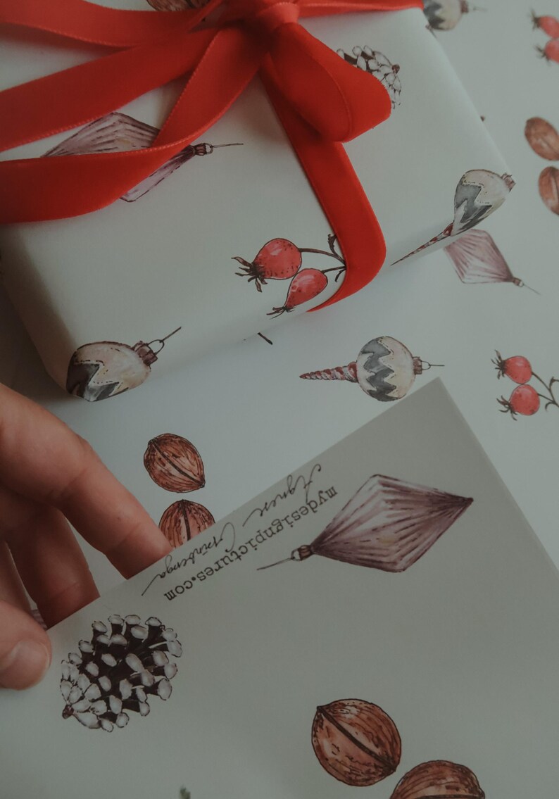 May include: White wrapping paper with a red ribbon tied in a bow. The paper has a repeating pattern of Christmas ornaments, pine cones, and red berries. The text "MyBestPrints.com" is printed on the paper.