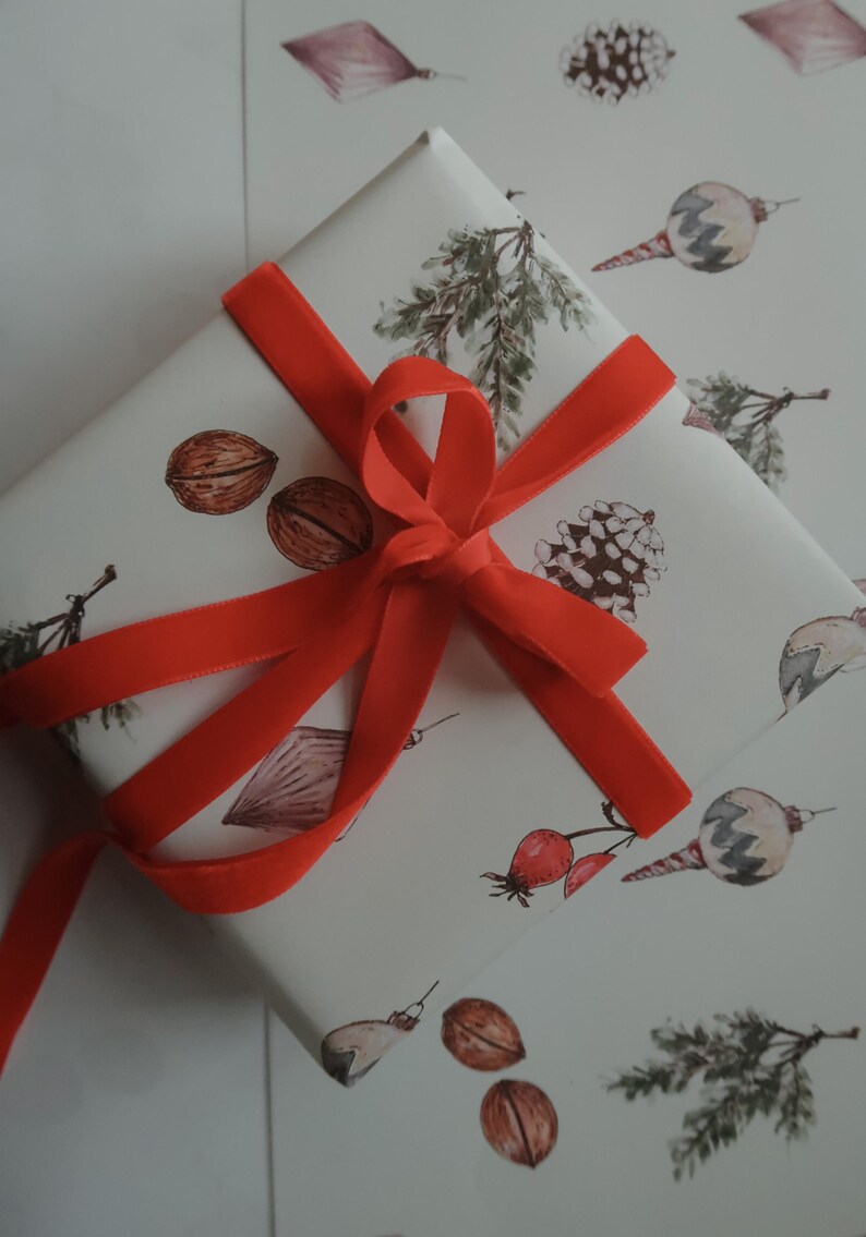 May include: A white gift box with a red ribbon tied in a bow. The box is wrapped in paper with a pattern of pine branches, nuts, berries, and ornaments.