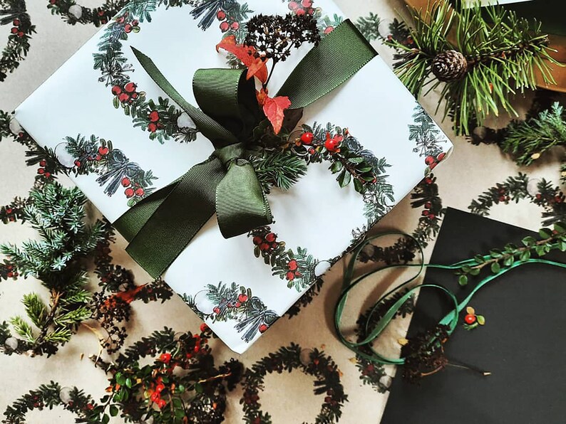 May include: White gift wrap with a green ribbon and a repeating pattern of green wreaths with red berries. The wreaths are on a brown background.