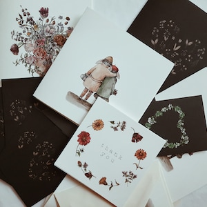 May include: A set of five cards with a floral design, a couple walking, and the words "thank you". The cards are white with black ink and are arranged in a fan shape.
