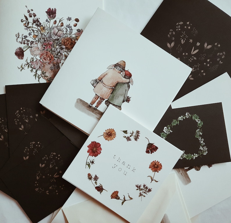May include: A set of five cards with a floral design, a couple walking, and the words "thank you". The cards are white with black ink and are arranged in a fan shape.