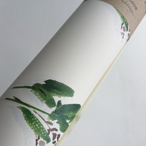 May include: A rolled up white paper with a green watercolor painting of leaves and branches. The paper is labeled "This Paper is A (50x70 cm) ...tempictures.com ...anden..."