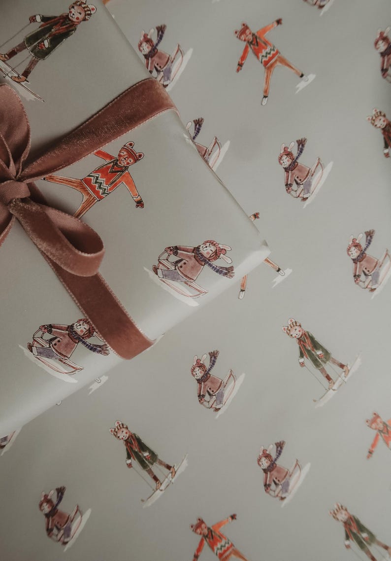 May include: Gift wrap featuring a repeating pattern of skiers in winter attire on a light gray background. A brown velvet ribbon is tied around a wrapped gift. The skiers are in various poses, wearing hats, scarves, and coats.