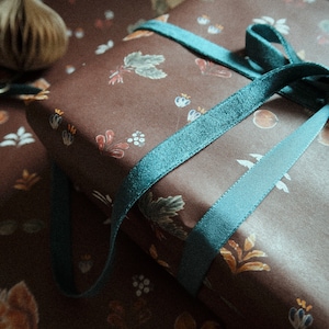 May include: A brown gift box with a teal ribbon tied in a bow. The box is wrapped in paper with a floral pattern.