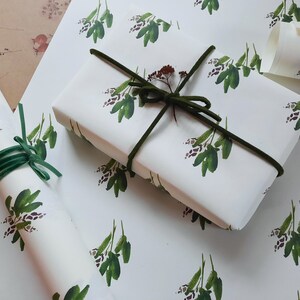 May include: White gift wrap with a repeating pattern of green leafy sprigs. The gift wrap is tied with a green ribbon.