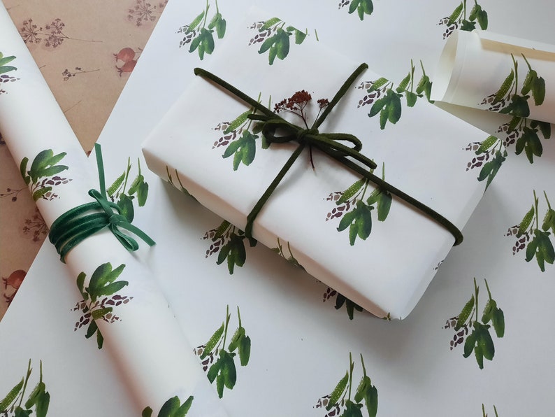May include: White gift wrap with a repeating pattern of green leafy sprigs. The gift wrap is tied with a green ribbon.
