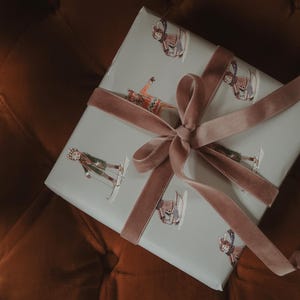 May include: A wrapped gift with light blue paper featuring skiers in various poses. The gift is tied with a dusty rose velvet ribbon and bow. The background is a dark orange-brown.