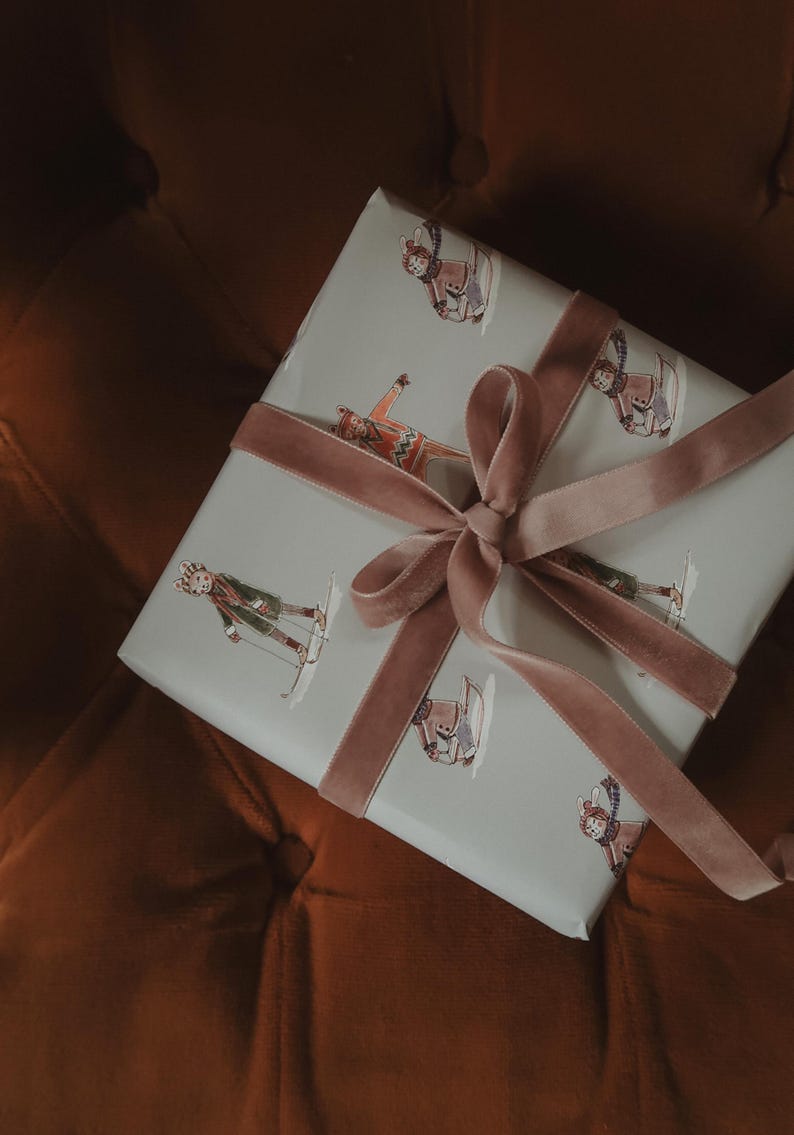 May include: A wrapped gift with light blue paper featuring skiers in various poses. The gift is tied with a dusty rose velvet ribbon and bow. The background is a dark orange-brown.