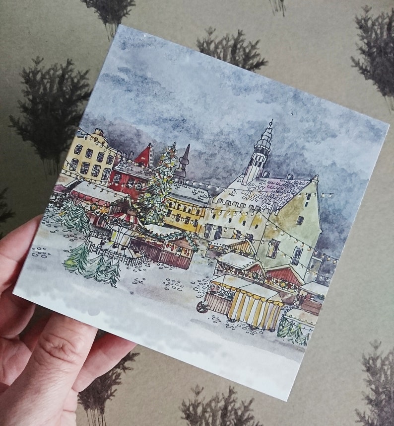 May include: Watercolor painting of a European Christmas market scene with a tall church steeple in the background. The market is filled with wooden stalls and decorated with twinkling lights. A large Christmas tree stands in the center of the scene.