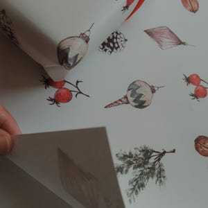 May include: White wrapping paper with a repeating pattern of watercolor illustrations. The illustrations include pine cones, holly berries, Christmas ornaments, and sprigs of greenery.