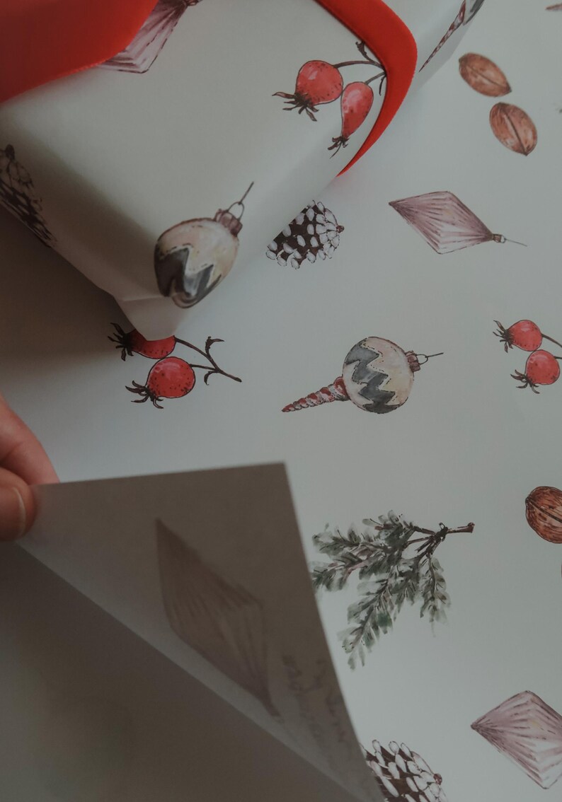 May include: White wrapping paper with a repeating pattern of watercolor illustrations. The illustrations include pine cones, holly berries, Christmas ornaments, and sprigs of greenery.