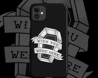 Puede incluir: Funda de teléfono negra con un diseño de ataúd blanco y el texto "WISH YOU WERE HERE" en una pancarta. El diseño es de estilo tatuaje, sobre un fondo oscuro con elementos de pancarta adicionales.