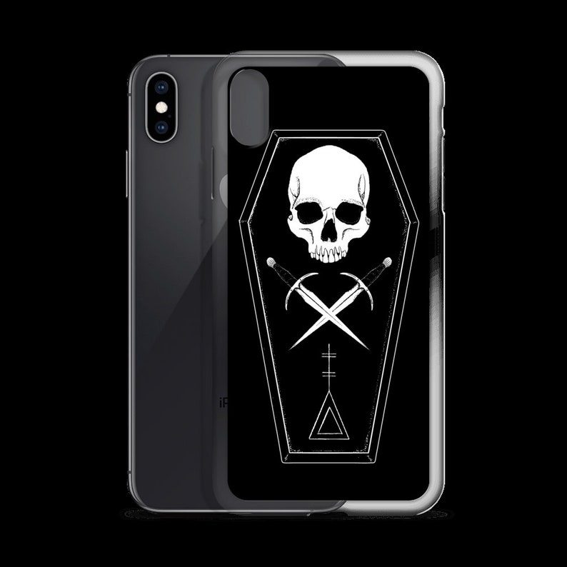 Puede incluir: Carcasa de tel&eacute;fono negra con un dise&ntilde;o de calavera blanca y espadas cruzadas dentro de una forma de ata&uacute;d. El dise&ntilde;o tambi&eacute;n incluye un tri&aacute;ngulo y una cruz.