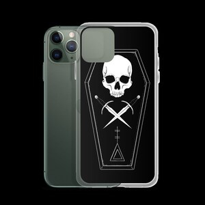 Puede incluir: Una funda de tel&eacute;fono negra con un dise&ntilde;o de calavera y huesos cruzados blancos dentro de un ata&uacute;d. El dise&ntilde;o tambi&eacute;n incluye un tri&aacute;ngulo y una cruz.