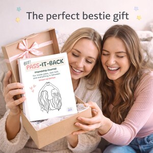 May include: A friendship journal titled "PASS-IT-BACK" is presented in a gift box with a pink ribbon. The journal cover features the text "BFF!" and "Friendship Journal" with a line drawing of two figures. The box is being opened by two smiling women.