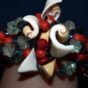 May include: A close-up of a bracelet made with various materials, including seashells, red and green beads, and blue crystals.