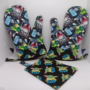 May include: A Star Wars-themed kitchen set featuring two oven mitts and a pot holder. The oven mitts and pot holder are black with a repeating pattern of Star Wars characters and logos. The set is designed for kitchen use.