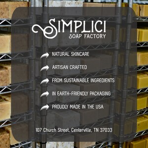 May include: A close-up of a shelf stocked with bars of handmade soap. The soap is made with natural ingredients and packaged in earth-friendly materials. The sign above the soap reads "SIMPLICI SOAP FACTORY". The sign also lists the company's values: "Natural Skincare", "Artisan Crafted", "From Sustainable Ingredients", "In Earth-Friendly Packaging", and "Proudly Made in the USA". The address of the soap factory is listed below the sign: "107 Church Street, Centerville, TN 37033".