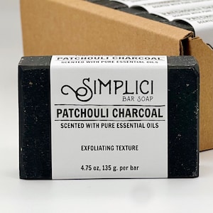 May include: A black bar of soap with white text that reads "PATCHOULI CHARCOAL SCENTED WITH PURE ESSENTIAL OILS SIMPLICI BAR SOAP PATCHOULI CHARCOAL SCENTED WITH PURE ESSENTIAL OILS EXFOLIATING TEXTURE 4.75 oz, 135 g. per bar"