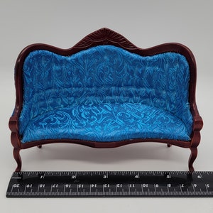 May include: Miniature sofa with a dark wood frame and a vibrant blue patterned fabric. The sofa has a curved back and armrests, and is approximately 6 inches long. A ruler is placed next to the sofa.