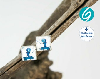 May include: A pair of silver stud earrings featuring a square blue and white illustration of a small figure sitting on a bench. The earrings are displayed on a piece of driftwood.